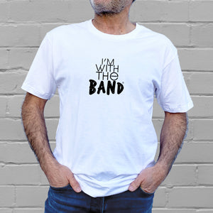 I'm With The Band® logo T-shirt with black print on white T being worn by a faceless man standing against a white painted brick wall