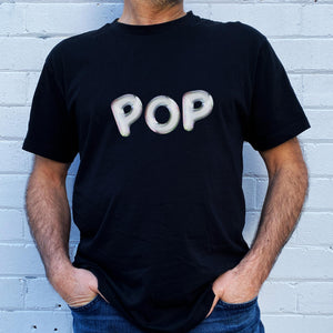 I'm With The Band® Bubble Pop T-shirt with iridescent white print on black T being worn by a faceless man standing against a white painted brick wall