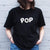I'm With The Band® Bubble Pop T-shirt with iridescent white print on black T being worn by a faceless woman standing against a white painted brick wall