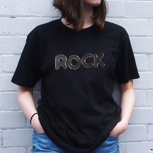 I'm With The Band® Bubble Rock T-shirt with black print on black T being worn by a faceless woman standing against a white painted brick wall