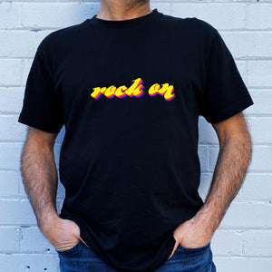 I'm With The Band® bright multi-colour Rock On T-shirt with white print on black T being worn by a faceless man standing against a white painted brick wall