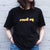 I'm With The Band® bright multi-colour Rock On T-shirt with white print on black T being worn by a faceless woman standing against a white painted brick wall