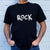 I'm With The Band® hand painted Rock T-shirt with white print on black T being worn by a faceless man standing against a white painted brick wall