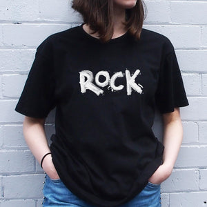 I'm With The Band® hand painted Rock T-shirt with white print on black T being worn by a faceless woman standing against a white painted brick wall