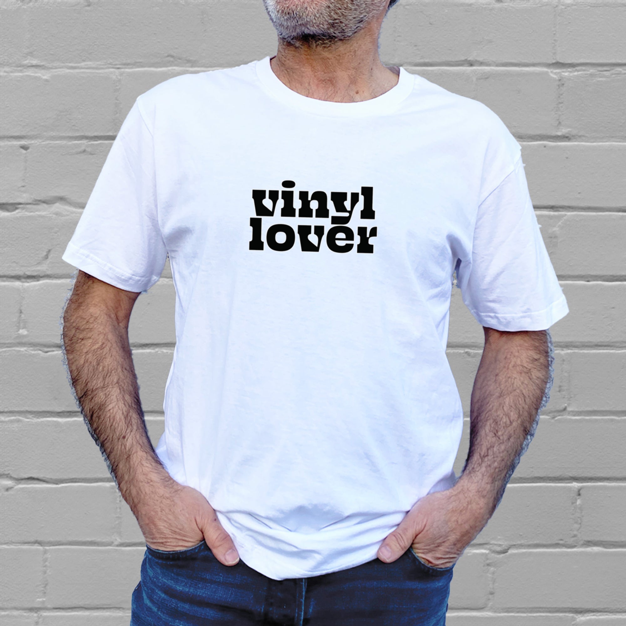I'm With The Band® Vinyl Lover T-shirt with bright multi-colour print on white T being worn by a faceless man standing against a white painted brick wall