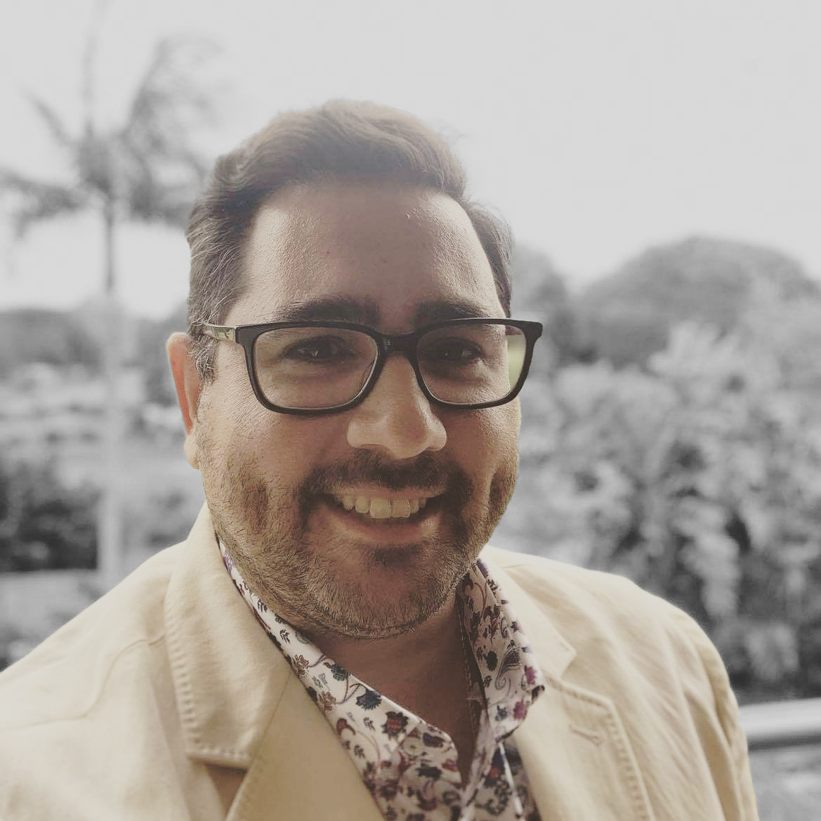 George is smiling at the camera. He is 30-something and is wearing black rimmed glasses.