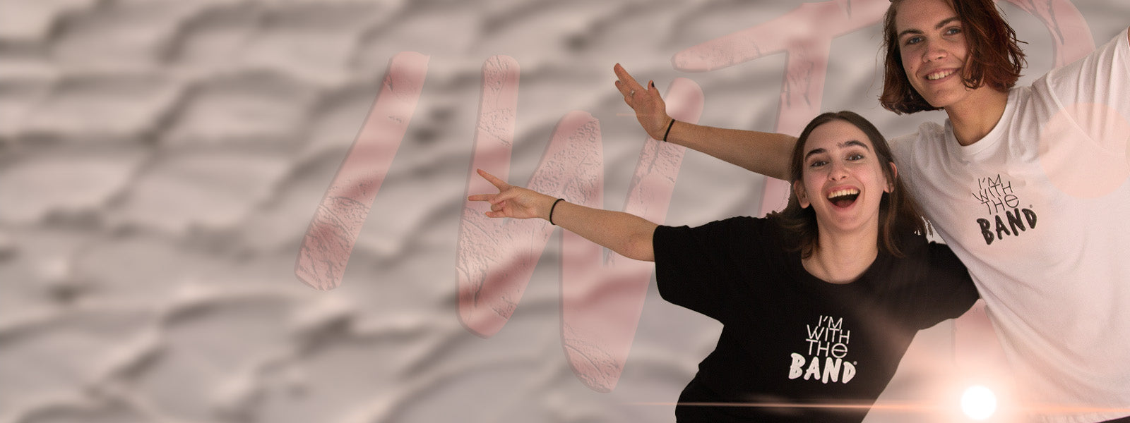 I'm With The Band - T-shirts for music - good vibes and music life apparel, black and white logo T-shirts modelled by a cool and happy young man and woman with arms outstretched and smiling at camera. They are in front of a graffiti style IWTB and blurred stucco background.