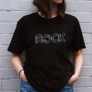 I'm With The Band® Bubble Rock T-shirt with iridescent oil slick grey print on black T being worn by a faceless woman standing against a white painted brick wall