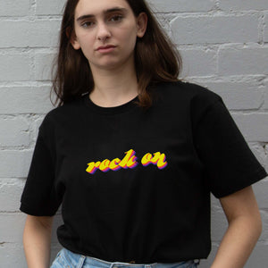 I'm With The Band® Rock On T-shirt with bright colour print on black T  on  cool young woman against a painted brick wall