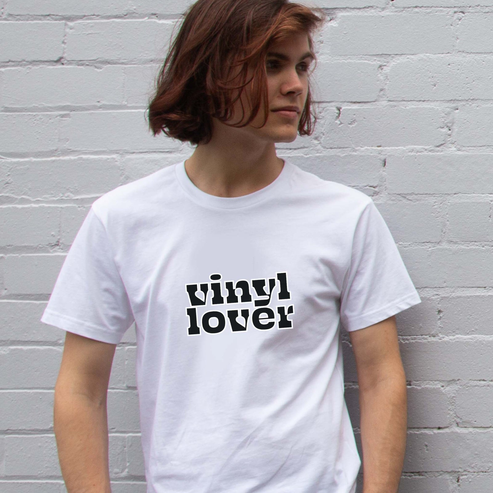 I'm With The Band® Vinyl Lover T-shirt with bright multi-colour print on white T being worn by a cool young man standing against a white painted brick wall